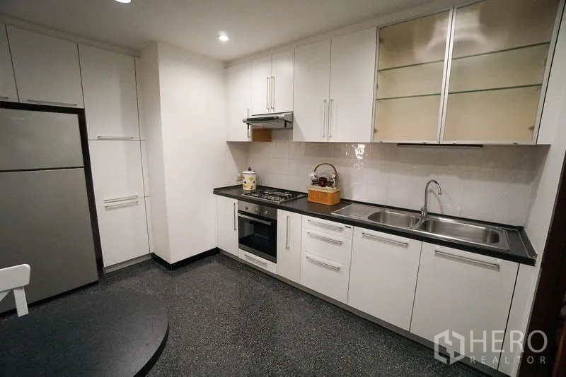 Apartment for rent in Watthana, Bangkok - Fitted white kitchen with gas hob, oven, ample cabinetry, and double sink.