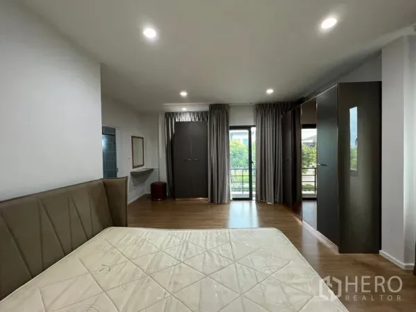 Detached House for rent in Saphan Sung, Bangkok - Spacious master bedroom with wood flooring, large bed, built‑in wardrobes and a balcony door with curtains.