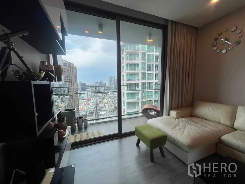 Condominium for rent in Khlong Toei, Bangkok - Living room with L-shaped sofa opening to a balcony and panoramic Bangkok skyline view.