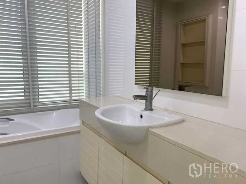 Condominium for rent in Khlong Toei, Bangkok - Bathroom with large mirror, vanity sink, blinds and a bathtub.