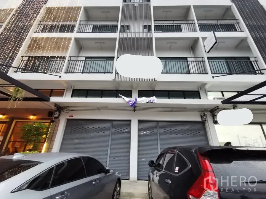 带办公室的家 出租在Suan Luang, Bangkok - 多层居家办公楼外立面，连排阳台与卷闸门门面，前方可停车