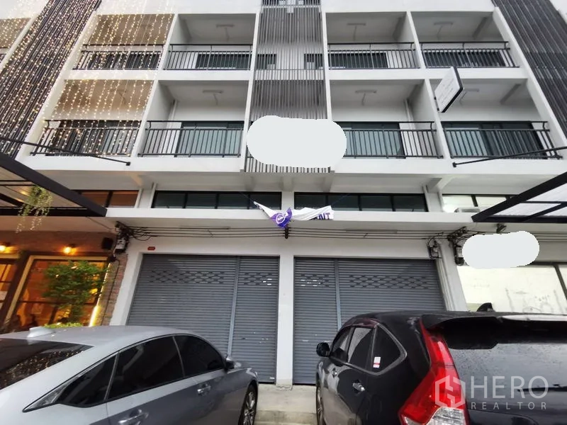 带办公室的家 出租在Suan Luang, Bangkok - 多层居家办公楼外立面，连排阳台与卷闸门门面，前方可停车