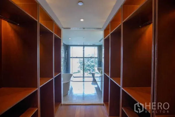 Condominium for rent in Yan Nawa, Bangkok - Walk-in closet with built-in wooden shelving opening to a bathroom with freestanding tub and shower.