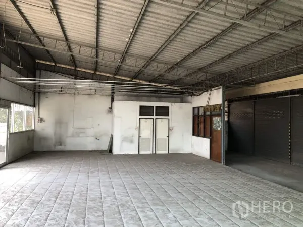 货栈 出租在Khlong Luang, Pathum Thani - 室内开放空间，铺砖地面与钢结构屋顶，带小型办公室门。