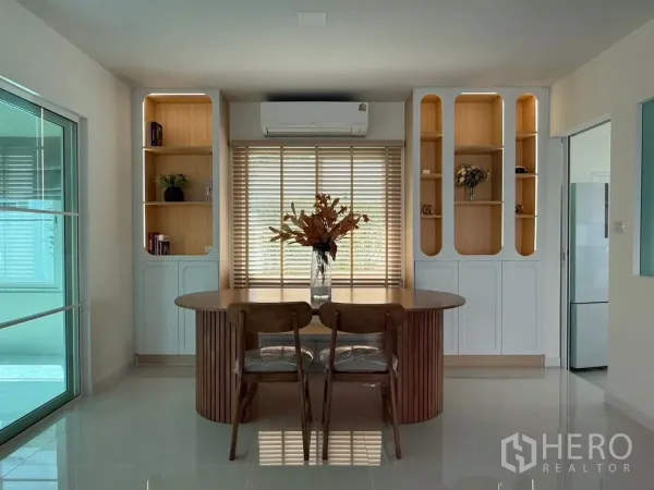 独立式住宅 出租在Bang Phli, Samut Prakan - 采光充足的餐/书房，圆形木桌、嵌入式书柜、百叶窗与空调，旁为玻璃移门。