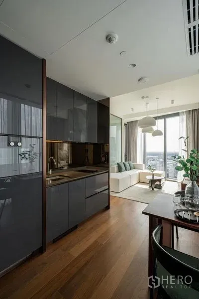 Condominium for rent in Khlong Toei, Bangkok - Sleek open kitchen with glossy cabinets, wood flooring and a dining nook leading to the living area.