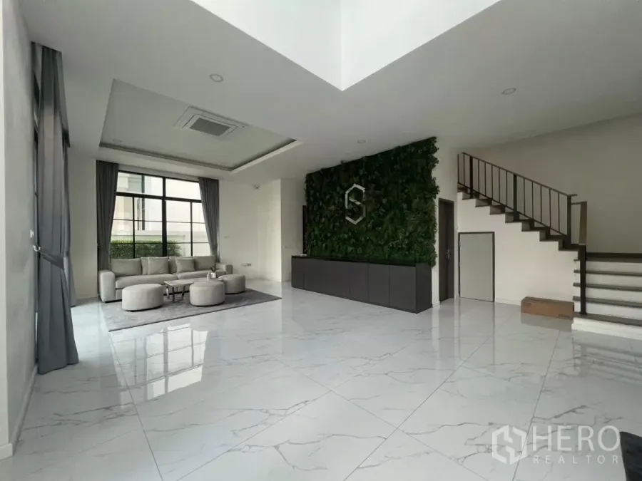 Detached House for rent in Lat Phrao, Bangkok - Bright living room with marble-look floors, large window, green feature wall and modern staircase in a detached house.
