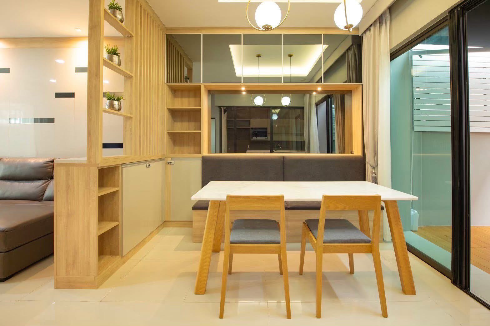 Townhouse for rent or sale in Lat Phrao, Bangkok - Dining area with marble-top table, bench seating, shelving and sliding doors to the patio.