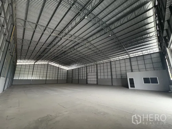 Warehouse for rent in Mueang Samut Prakan, Samut Prakan - Expansive warehouse interior with high steel truss roof, polished concrete floor, and a small internal office box.