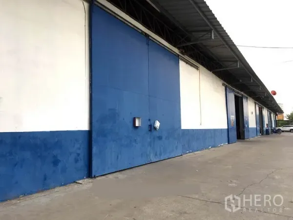 货栈 出租在Bang Phli, Samut Prakan - 蓝白色仓库外立面，超大滑动钢门与带顶装卸区，前方为宽阔混凝土通道，位于邦普里。