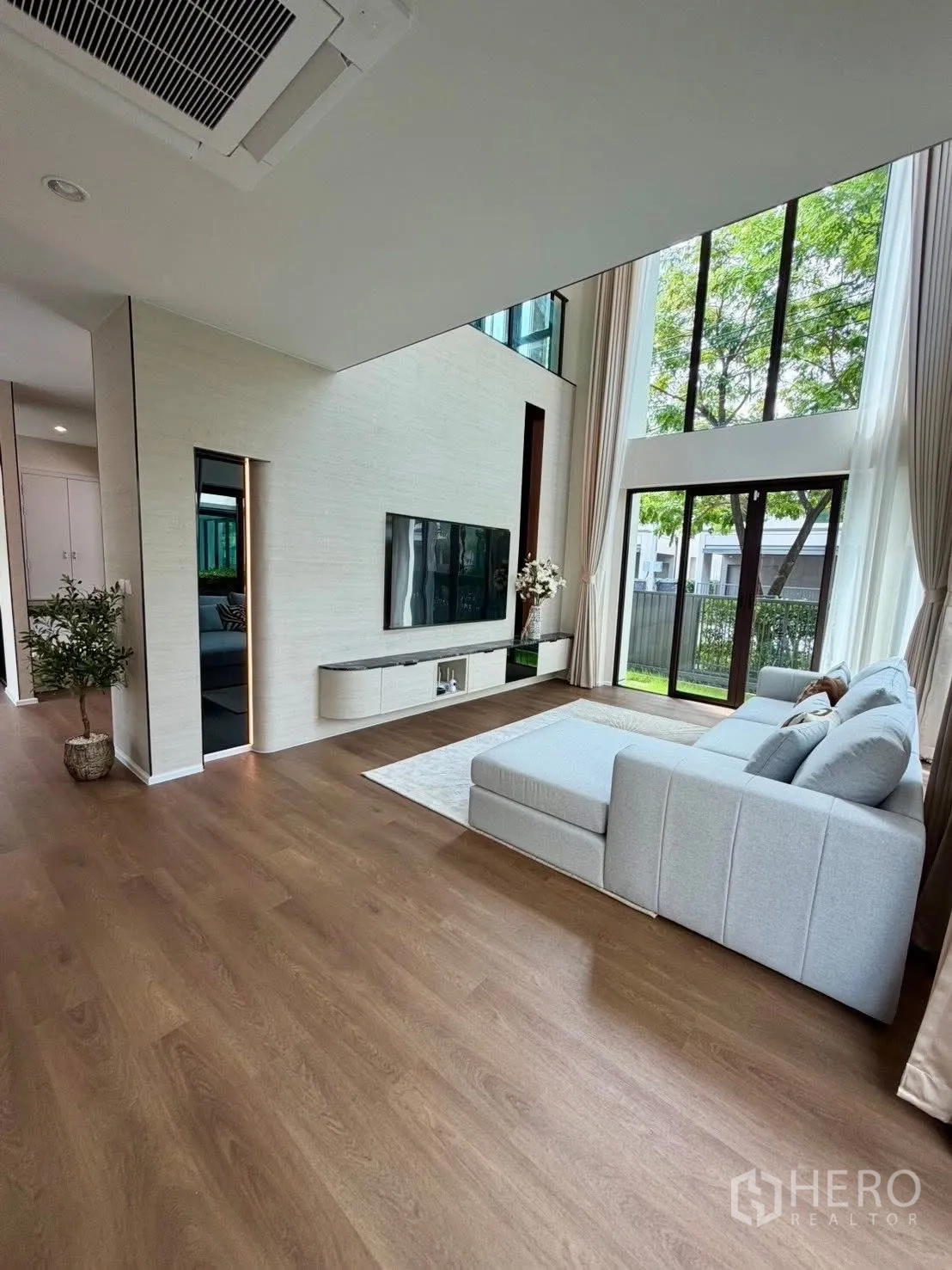 บ้านเดี่ยว for rent in Bang Phli, Samut Prakan - ห้องนั่งเล่นกว้าง ผนังทีวี โซฟารูปตัวแอล และกระจกสูงมองออกสู่สนามหญ้า