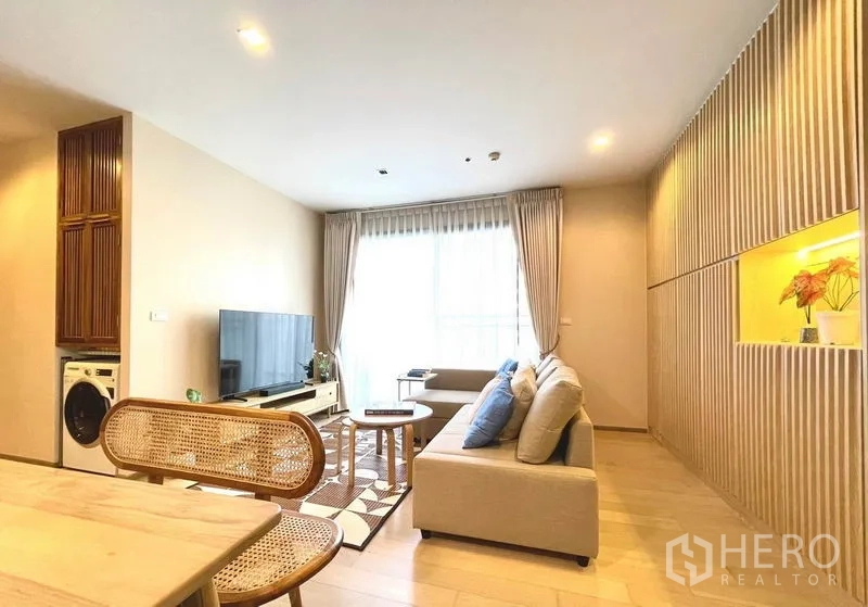 Condominium for rent or sale in Watthana, Bangkok - Living room angle showing TV, sofa, balcony light and a laundry niche with washer.
