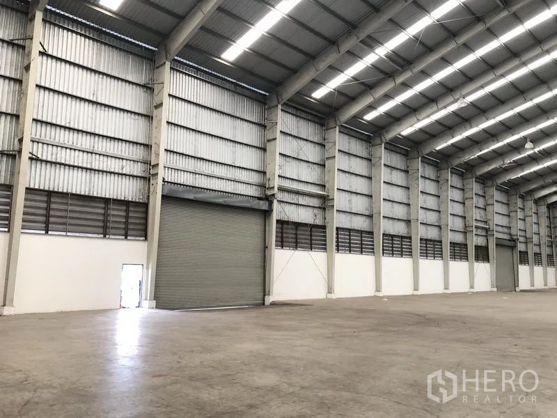 Warehouse for rent in Phra Nakhon Si Ayutthaya - Interior wall with large roller shutter door, ventilation louvres and heavy-duty concrete floor.