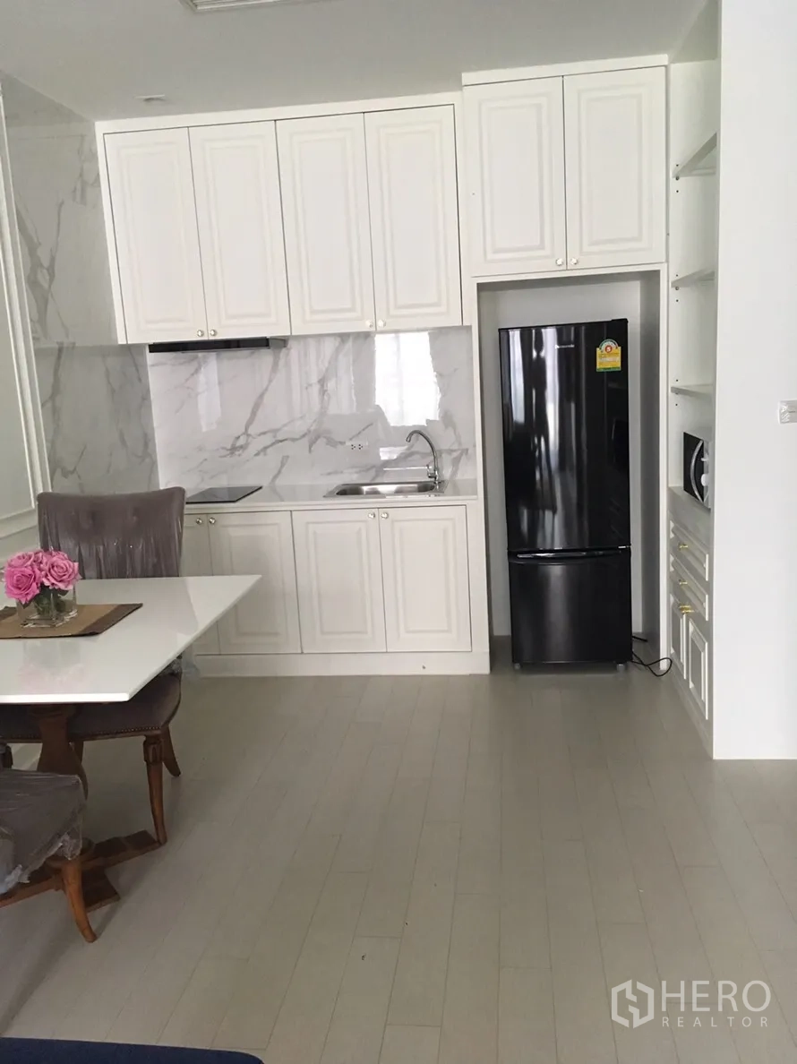 Condominium for rent in Pathum Wan, Bangkok - Compact white kitchen with marble backsplash, dining nook, and a black refrigerator.