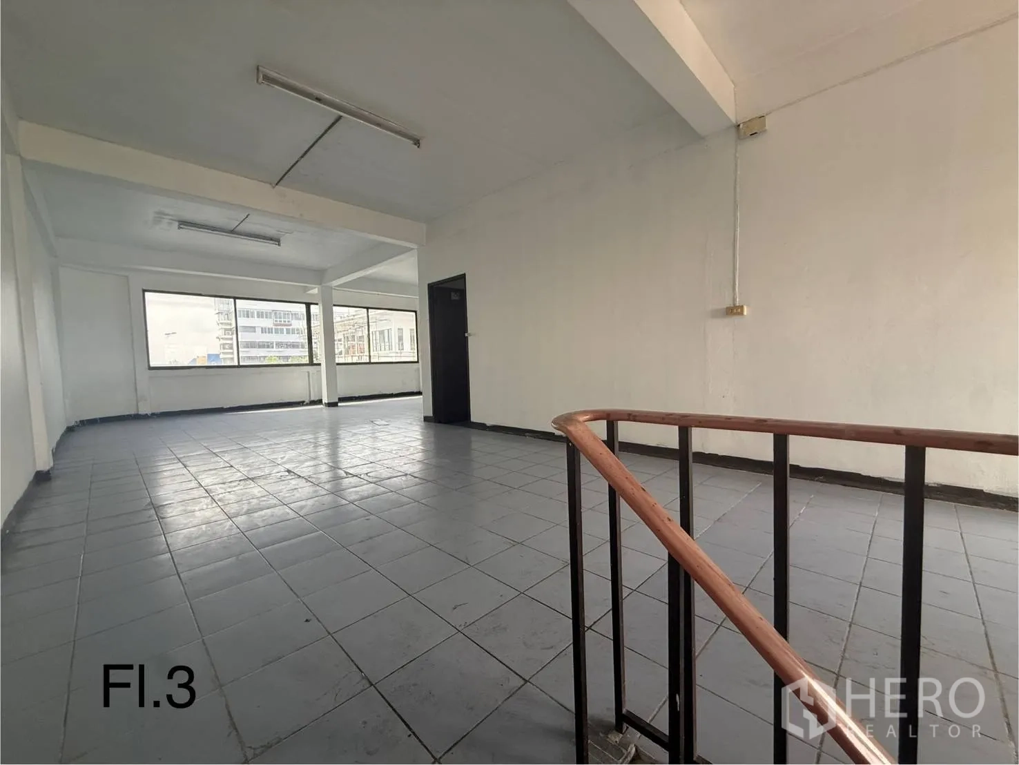 Shophouse for rent in Bang Na, Bangkok - Third-floor open office space with grey tiles, large corner windows, and stair railing.