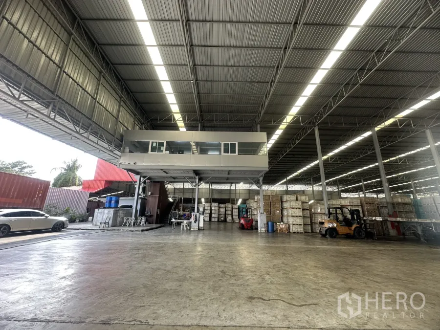 Warehouse for rent in Bang Yai, Nonthaburi - Warehouse bay with mezzanine office, forklifts, stacked pallets and wide covered loading area.
