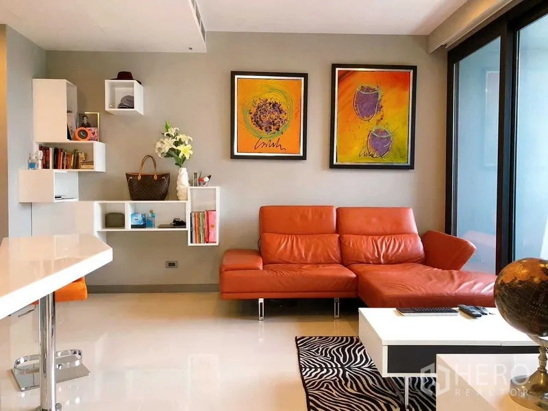 Condominium for rent in Bang Rak, Bangkok - Bright lounge with orange leather sectional, wall art and floating shelves.