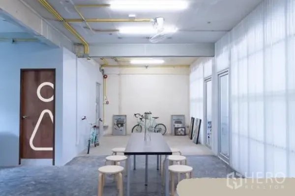 办公空间 出租在Phaya Thai, Bangkok - 极简工业风公共区，长桌与圆凳，外露管线与半透明隔断墙。