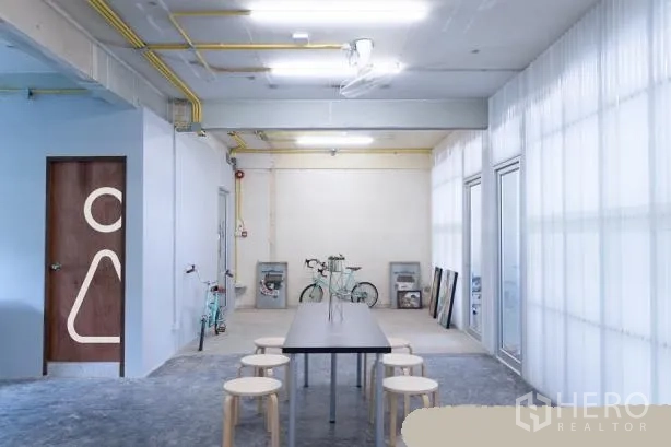 办公空间 出租在Phaya Thai, Bangkok - 极简工业风公共区，长桌与圆凳，外露管线与半透明隔断墙。