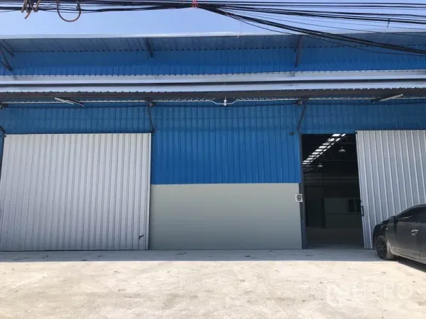 Warehouse for rent in Nonthaburi - Blue metal-clad warehouse exterior with wide sliding doors and loading apron in Pak Kret, Nonthaburi.