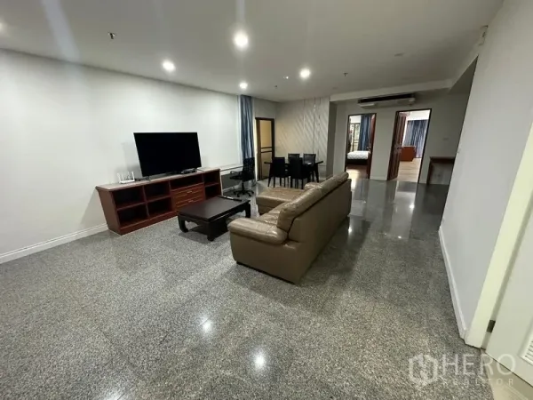 Condominium for rent in Watthana, Bangkok - Spacious living room with leather sofa, TV console, dining set, and glossy stone flooring.