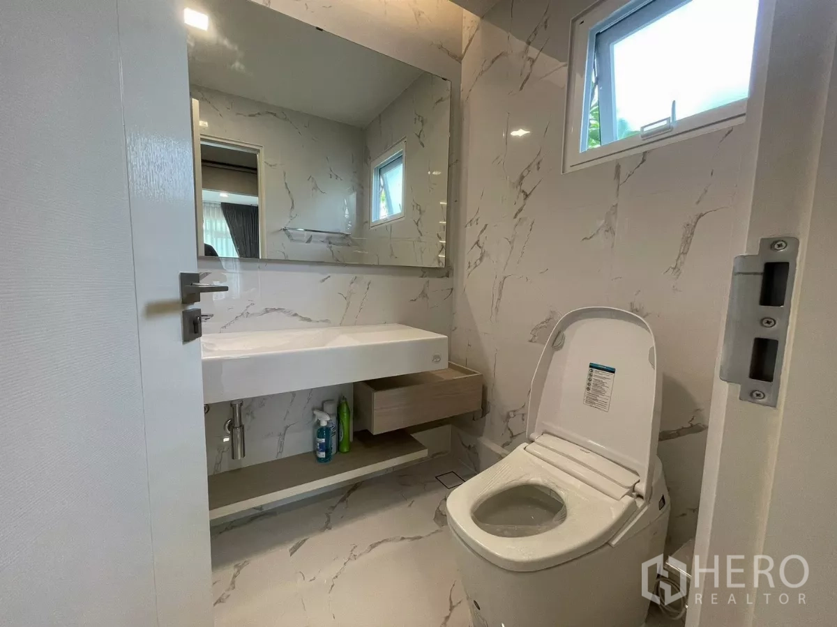 Detached House for rent in Prawet, Bangkok - Modern bathroom with marble-look tiles, large mirror, vanity and toilet.