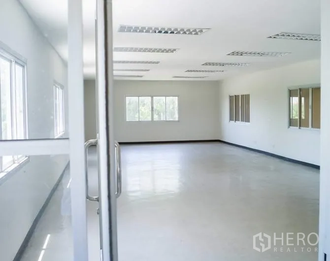 Factory for rent in Pathum Thani - Bright office room with large windows, white walls, and fluorescent ceiling lights.