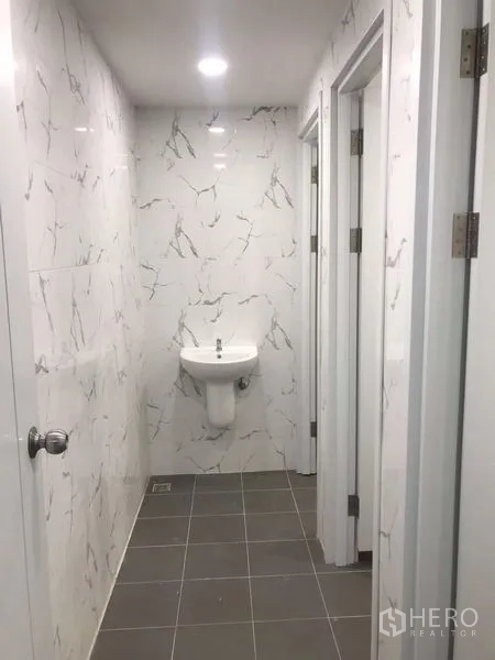 货栈 出租或出售在Nong Chok, Bangkok - 现代卫浴走廊，仿大理石墙砖、灰色地砖与挂墙式洗手盆。