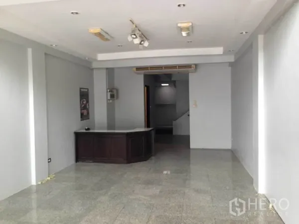 带办公室的家 出租或出售在Wang Thonglang, Bangkok - 一层开放式办公区，设接待台、灰色墙面、嵌入式灯具和后方楼梯。