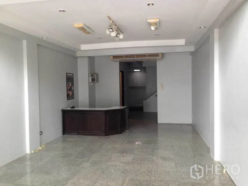 带办公室的家 出租或出售在Wang Thonglang, Bangkok - 一层开放式办公区，设接待台、灰色墙面、嵌入式灯具和后方楼梯。