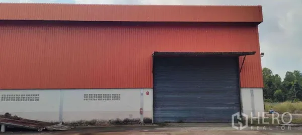 Warehouse for rent in Nikhom Phatthana, Rayong - Front facade of the warehouse with large roller shutter door, canopy and paved truck access.