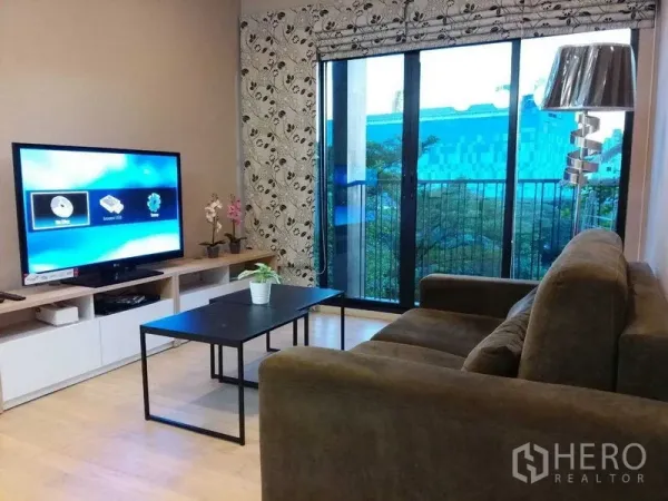 Condominium for sale in Watthana, Bangkok - Living room with sofa, TV console and sliding doors leading to the balcony.