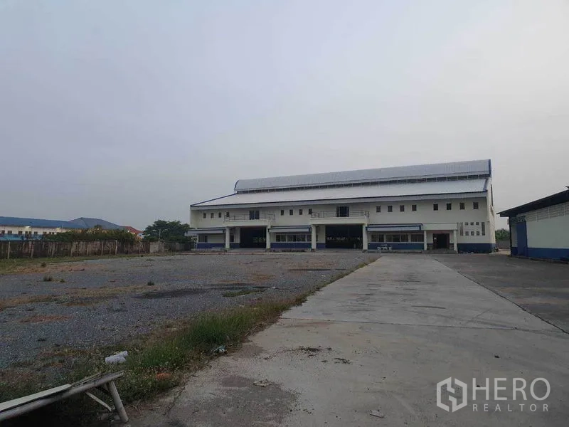 Factory for rent in Bang Bua Thong, Nonthaburi - Front of a large factory building with multiple loading bays and an expansive yard.
