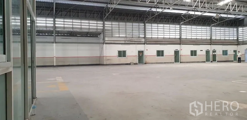 Warehouse for rent in Lam Luk Ka, Pathum Thani - Interior angle showing open floor area and a glass office partition near the loading zone.