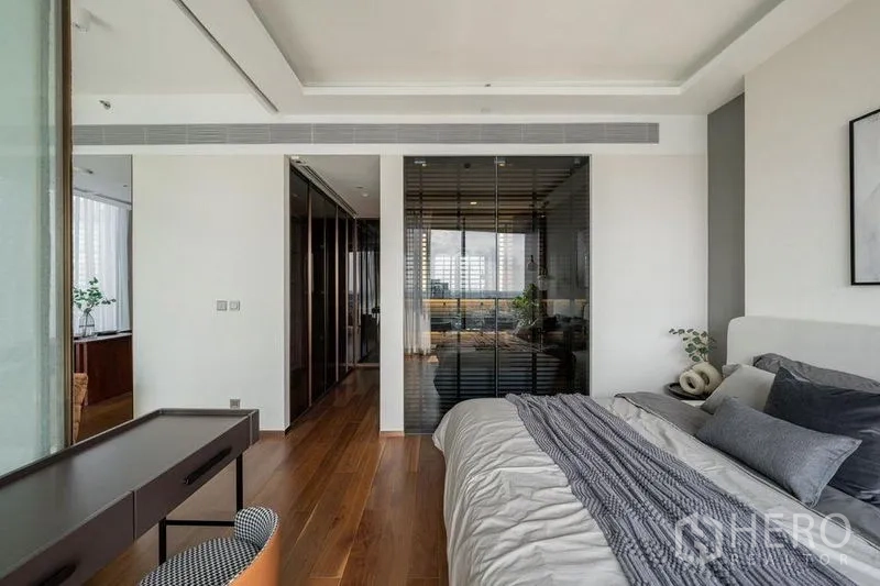 Condominium for rent in Khlong Toei, Bangkok - Primary bedroom showing wardrobe corridor and tinted glass partition set on warm wood floors.