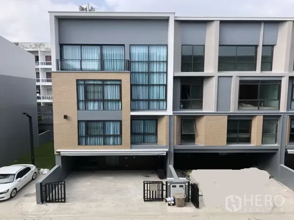 Townhouse for rent in Suan Luang, Bangkok - Contemporary multi-level townhouse facade with large windows, gated driveway and covered parking in a secure community.