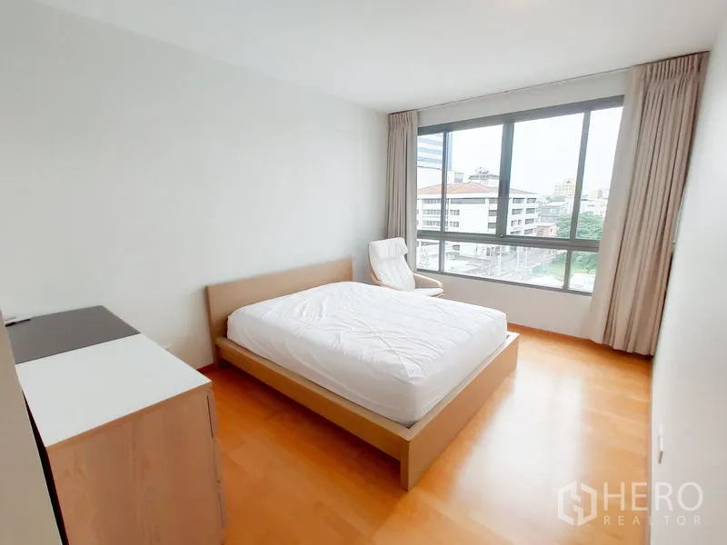 Condominium for rent in Khlong Toei, Bangkok - Sunlit master bedroom with city view through wide windows and a lounge chair.