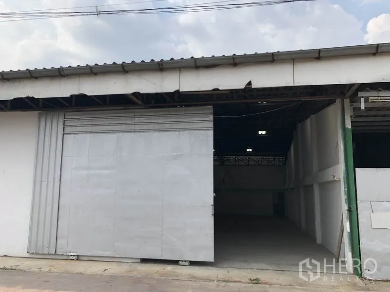 Warehouse for rent or sale in Khlong Luang, Pathum Thani - Front exterior of single-storey warehouse with wide metal sliding door and covered loading entry.