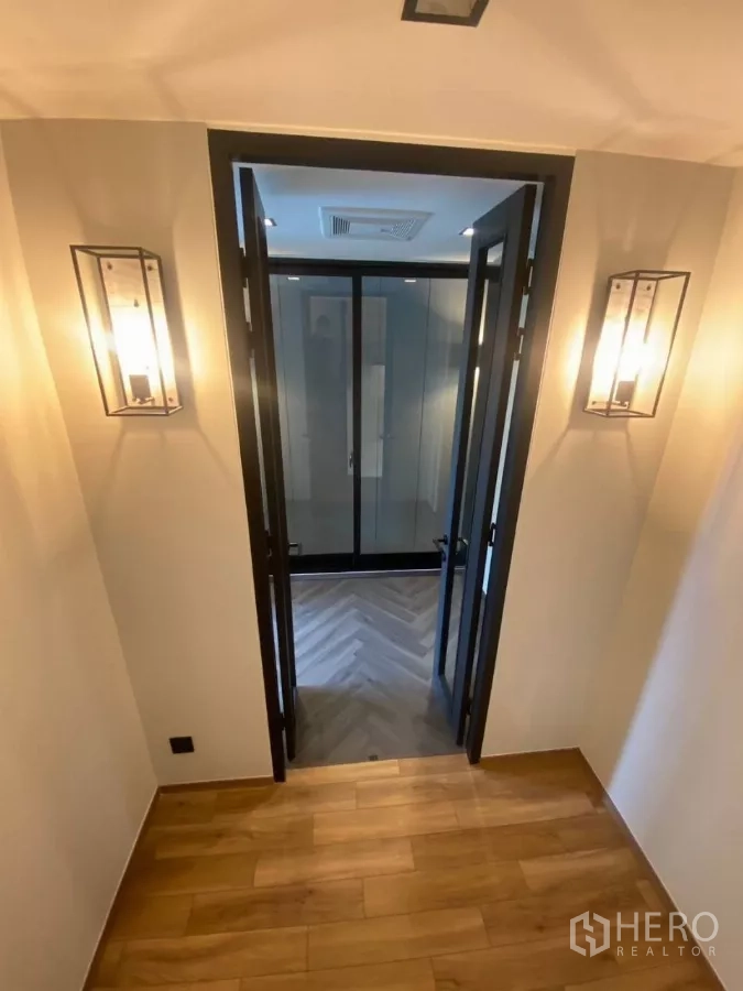 Townhouse for rent in Huai Khwang, Bangkok - Hallway with wall sconces leading to double glass doors and a herringbone floor room.