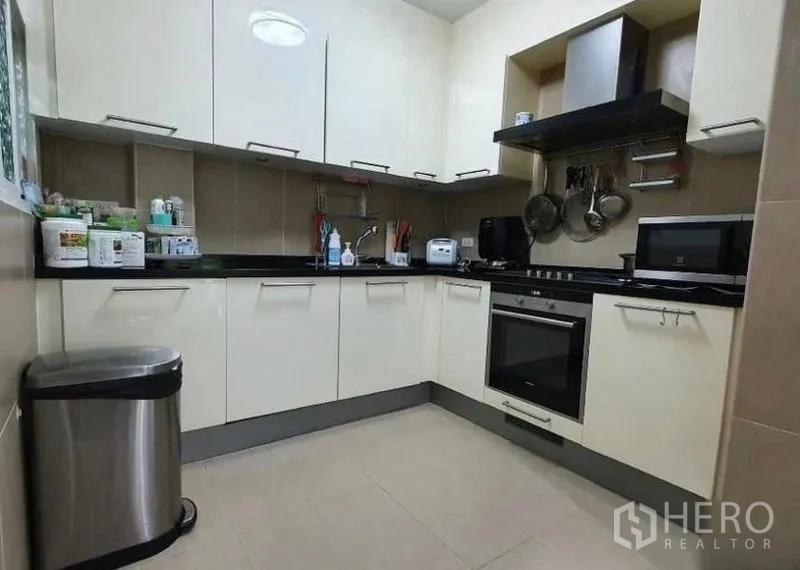 Detached House for rent or sale in Lat Krabang, Bangkok - Fitted L-shaped kitchen with upper and lower cabinets, oven, cooktop and range hood.