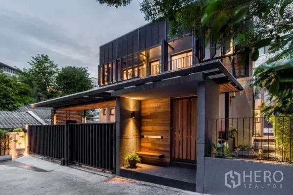 Townhouse for rent in Khlong Toei, Bangkok - Modern two-storey townhouse exterior at dusk with wood-and-metal facade, secure gate and warm lighting.