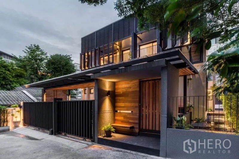 ทาวน์เฮาส์ ให้เช่าในKhlong Toei, Bangkok - ด้านหน้าทาวน์เฮาส์สไตล์โมเดิร์นสองชั้นยามเย็น ฟาซาดไม้และโลหะพร้อมรั้วปลอดภัยและไฟสว่าง