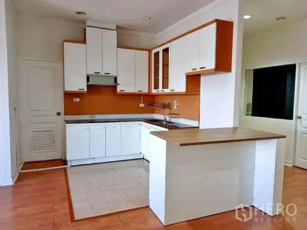 Condominium for rent in Khlong Toei, Bangkok - L-shaped kitchen with white cabinetry and a peninsula countertop over tile and wood flooring.