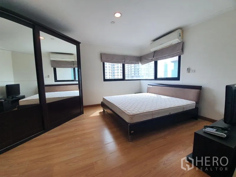 Condominium for rent in Sathon, Bangkok - Master bedroom with corner windows, mirrored wardrobe, air-conditioning and wood flooring.