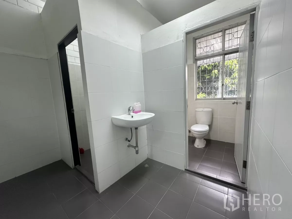 Warehouse for rent in Phra Khanong, Bangkok - Clean restroom with tiled walls, sink and toilet adjacent to the office area.