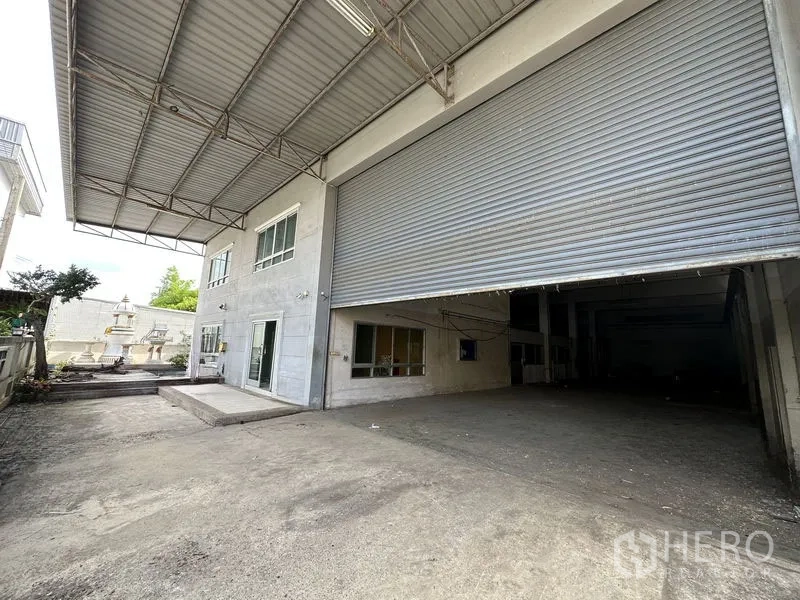 Factory for rent or sale in Bang Bua Thong, Nonthaburi - Covered loading bay with oversized roll-up door and two-storey office facade at the factory entrance.