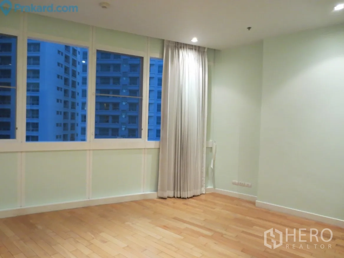 Condominium for rent in Khlong Toei, Bangkok - Corner bedroom with wood flooring, wide windows and curtains overlooking nearby high‑rises at dusk.