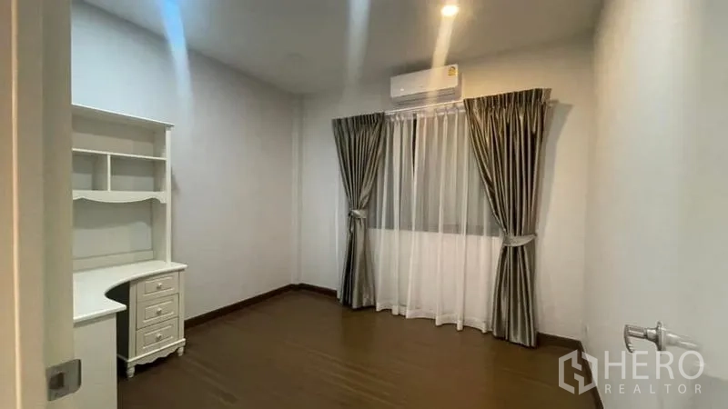 Detached House for rent or sale in Prawet, Bangkok - Quiet bedroom or study with built-in desk, wood flooring and curtains.