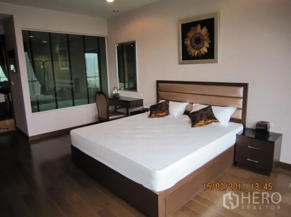 Condominium for rent or sale in Pathum Wan, Bangkok - Spacious bedroom angle showing bed, bedside tables, work desk, and window to bathroom with blinds.