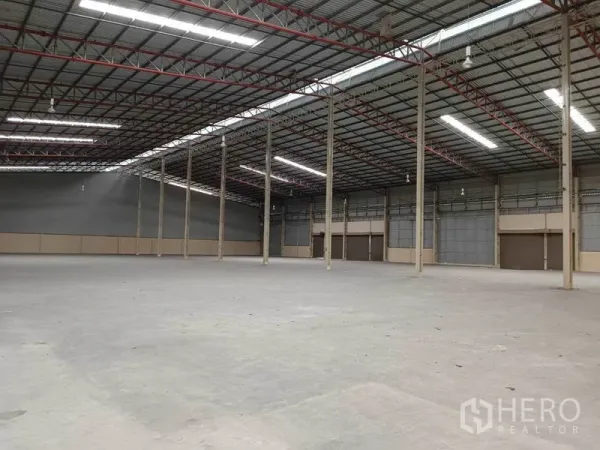 Factory for rent in Samut Prakan - Open factory interior with steel structure, ventilated wall panels, smooth concrete flooring and several large roll-up loading doors.